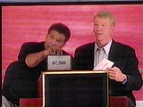 Greg Gumbel and Phil Simms show a '99 contestant his possible prize